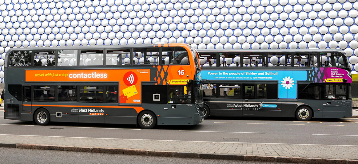 Two buses drivnig down a street.